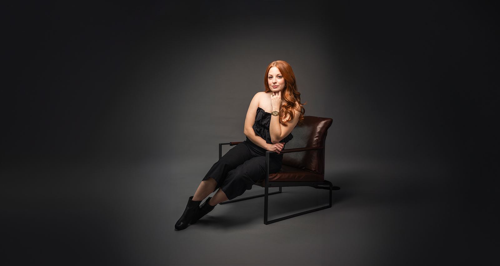 Model seated in a leather chair on a dark set