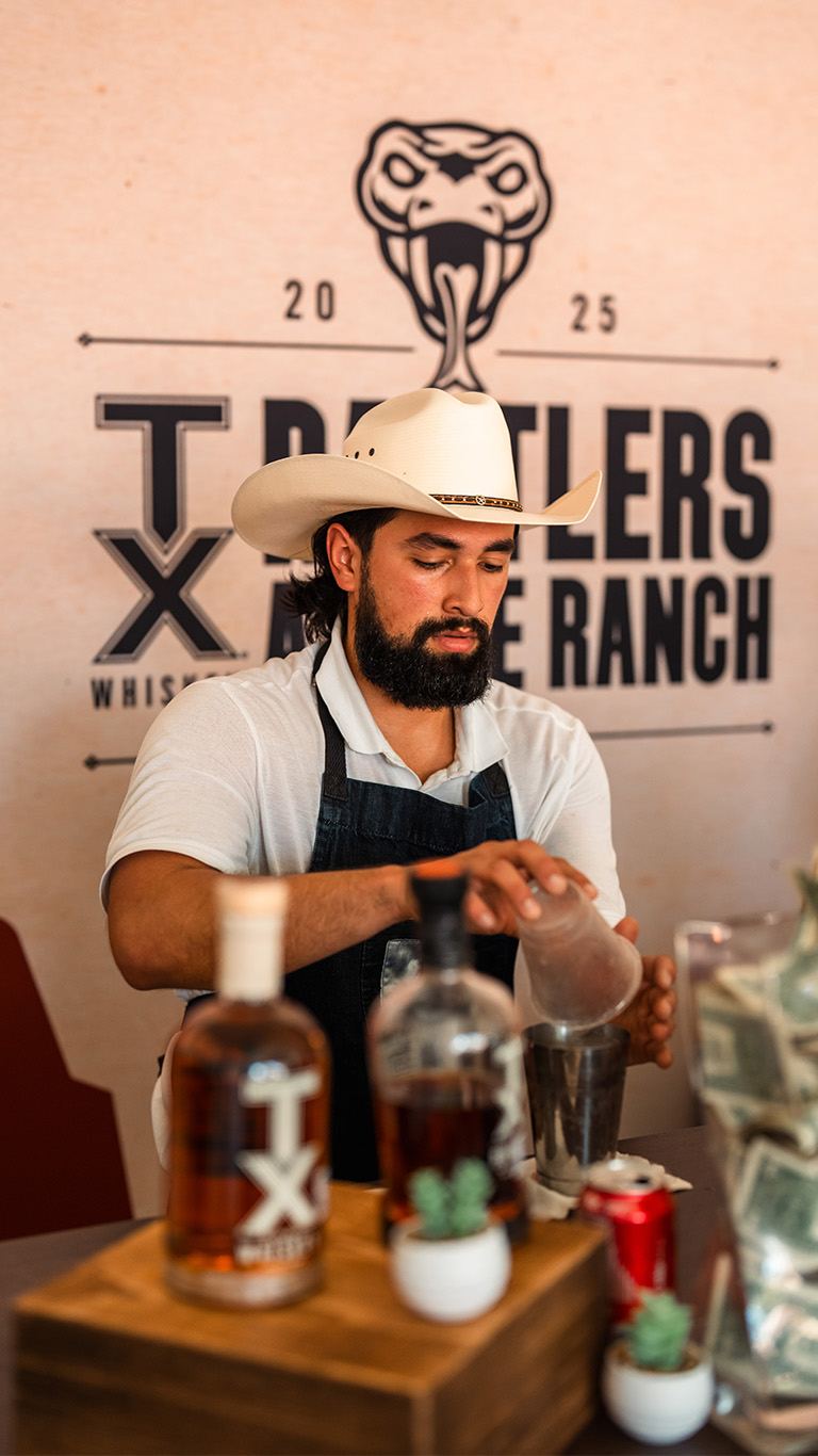 Bartender in a cowboy hat mixing drinks at a distillery booth
