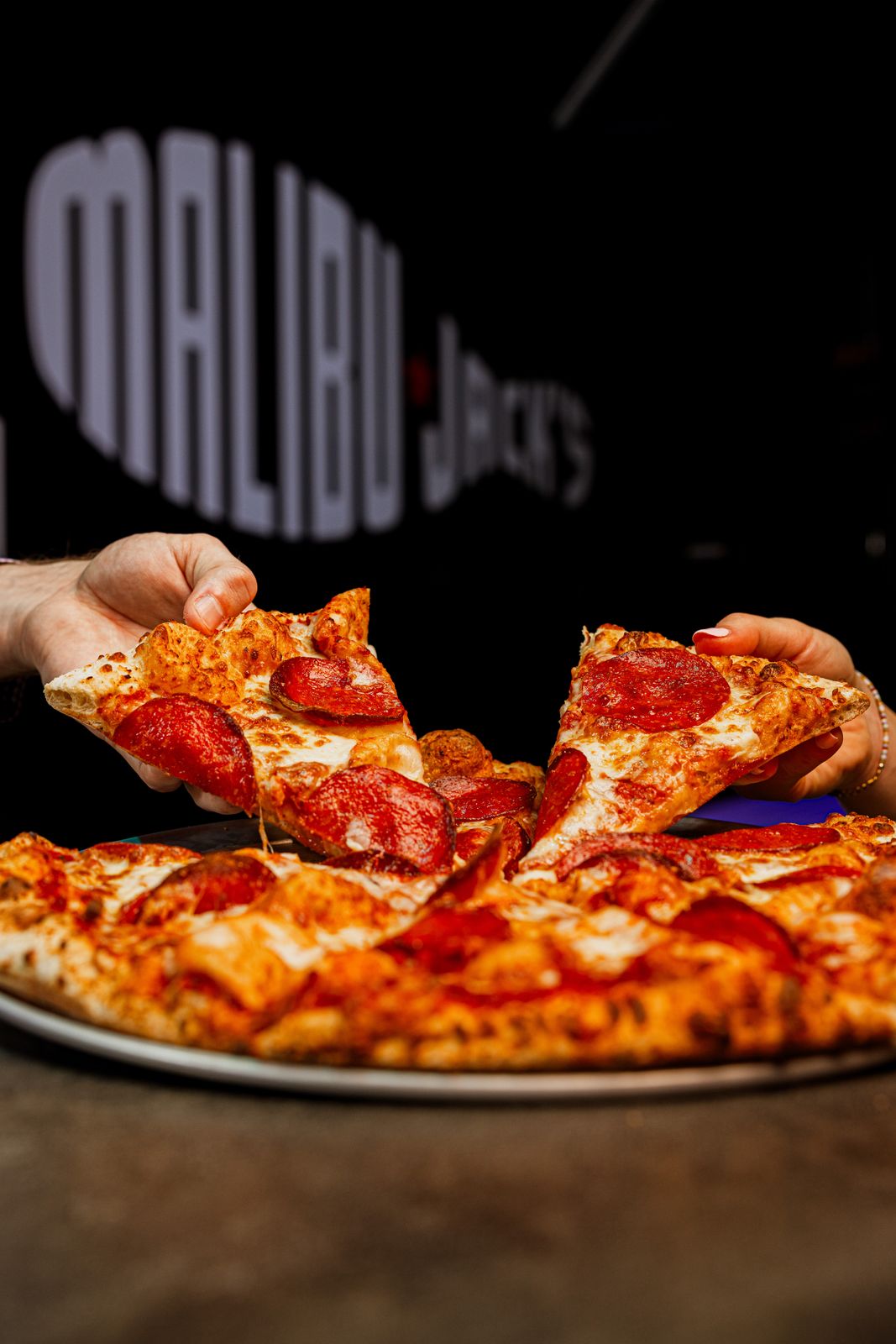 Hands pulling a slice of pepperoni pizza
