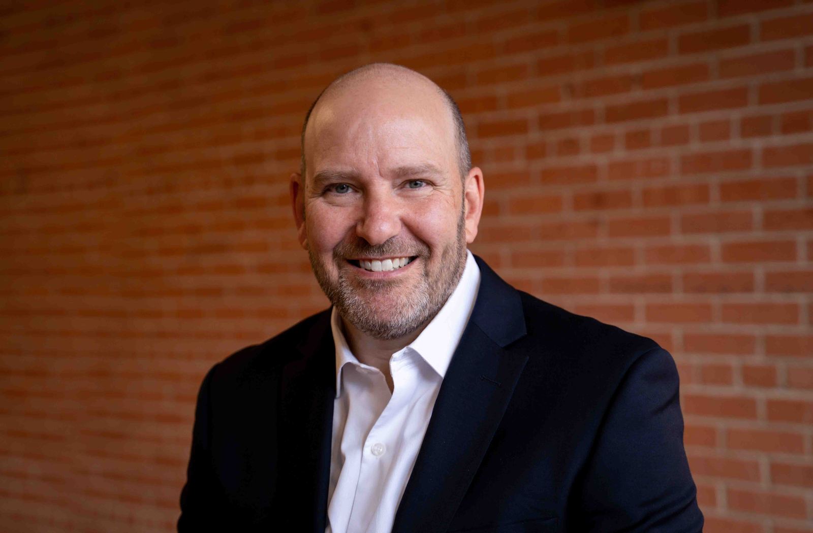 Headshot of a smiling man in a blazer against a brick wall