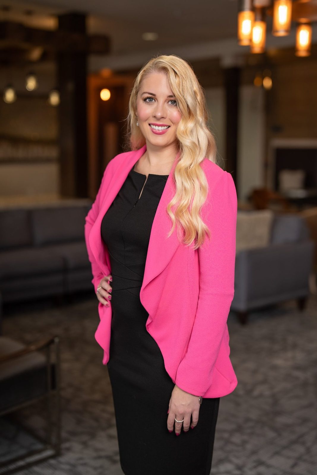 Professional headshot of a woman in a pink blazer in a warm lobby
