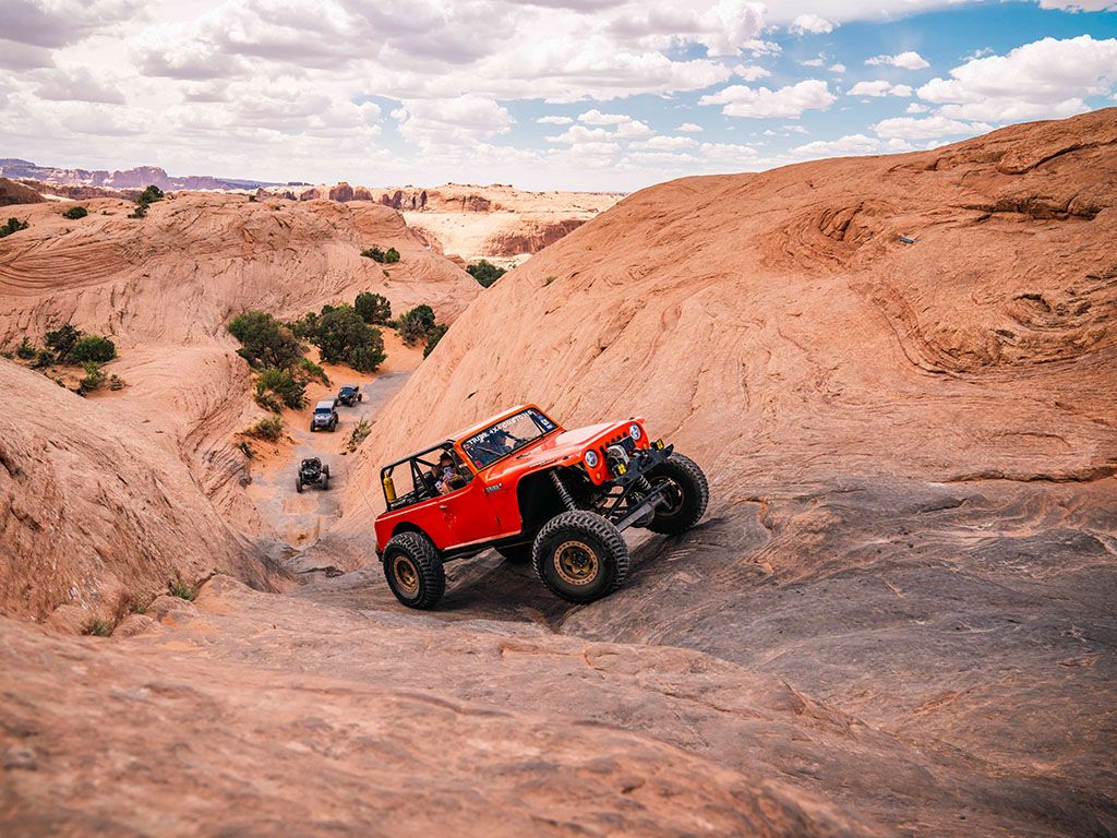 Red Jeep climbing desert slickrock