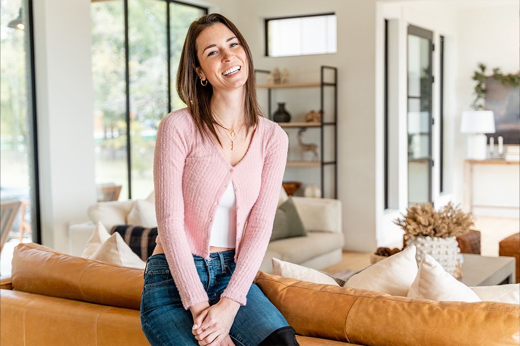 Woman seated on the arm of a sofa in a sunlit living room