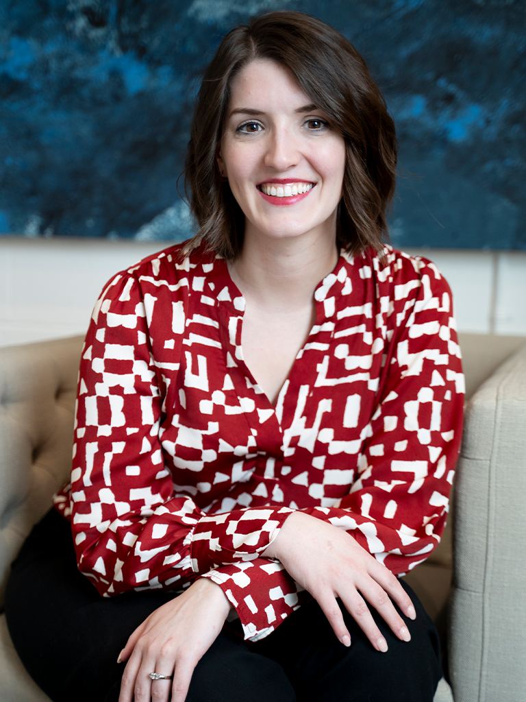 Smiling woman in a red patterned blouse seated in a living room