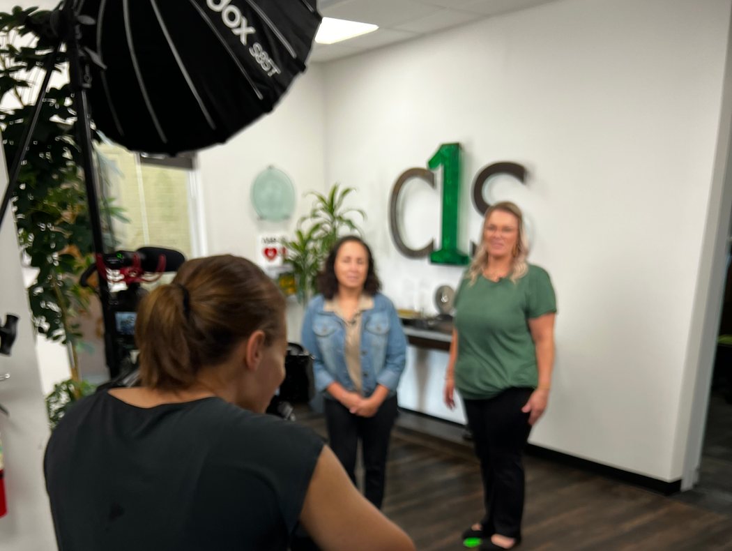 Susie Burleson directing two C1S team members in front of the C1S logo wall