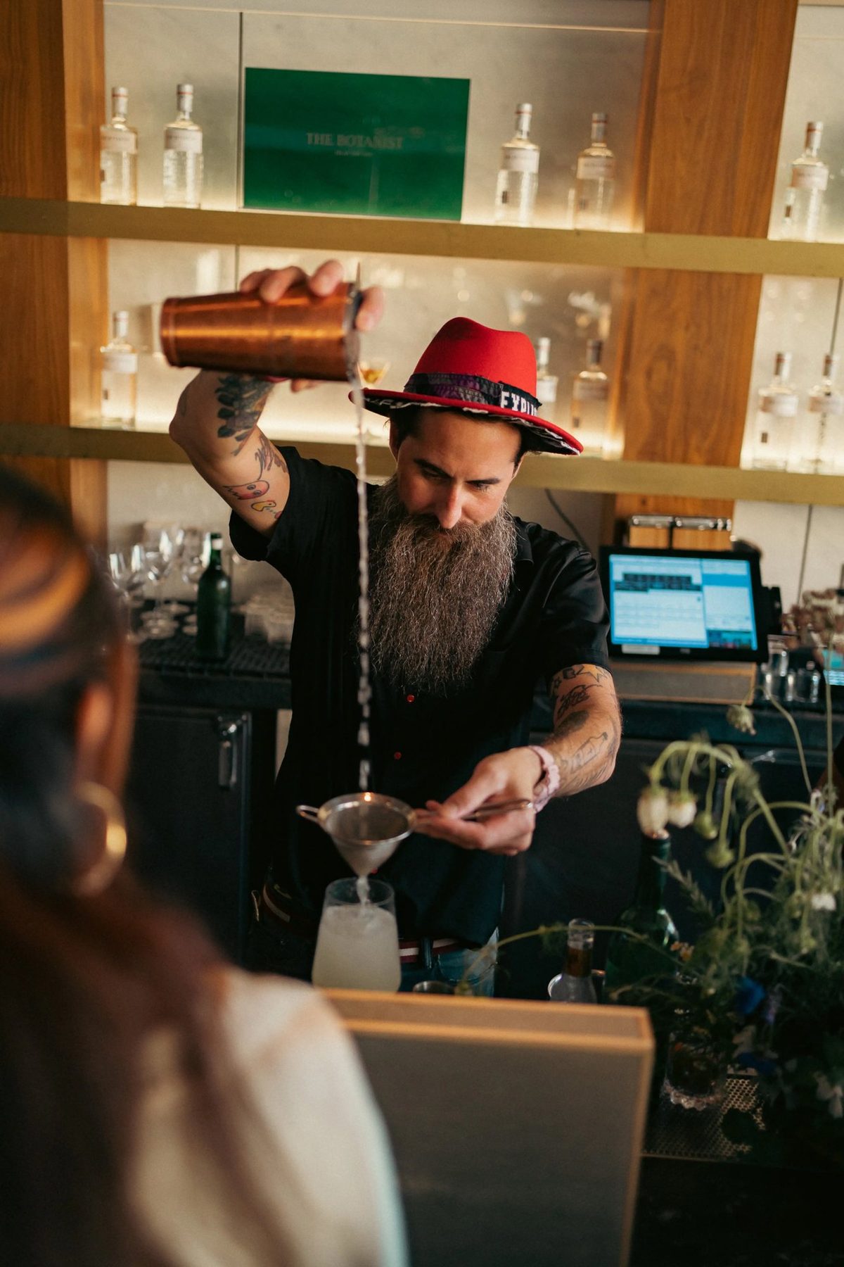 Mixologist in a red hat pouring a gin cocktail