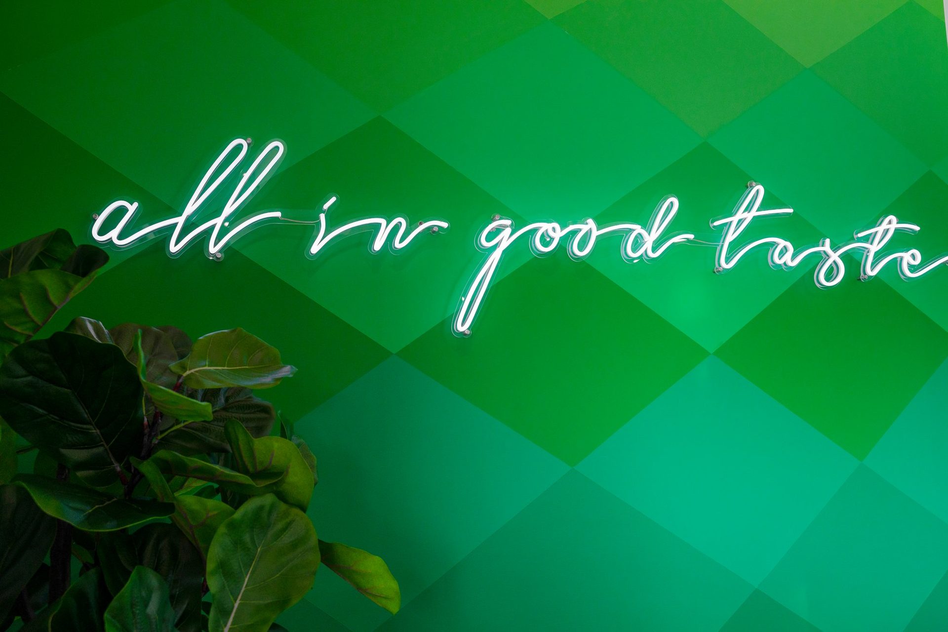 Green wall with the neon script "all in good taste"