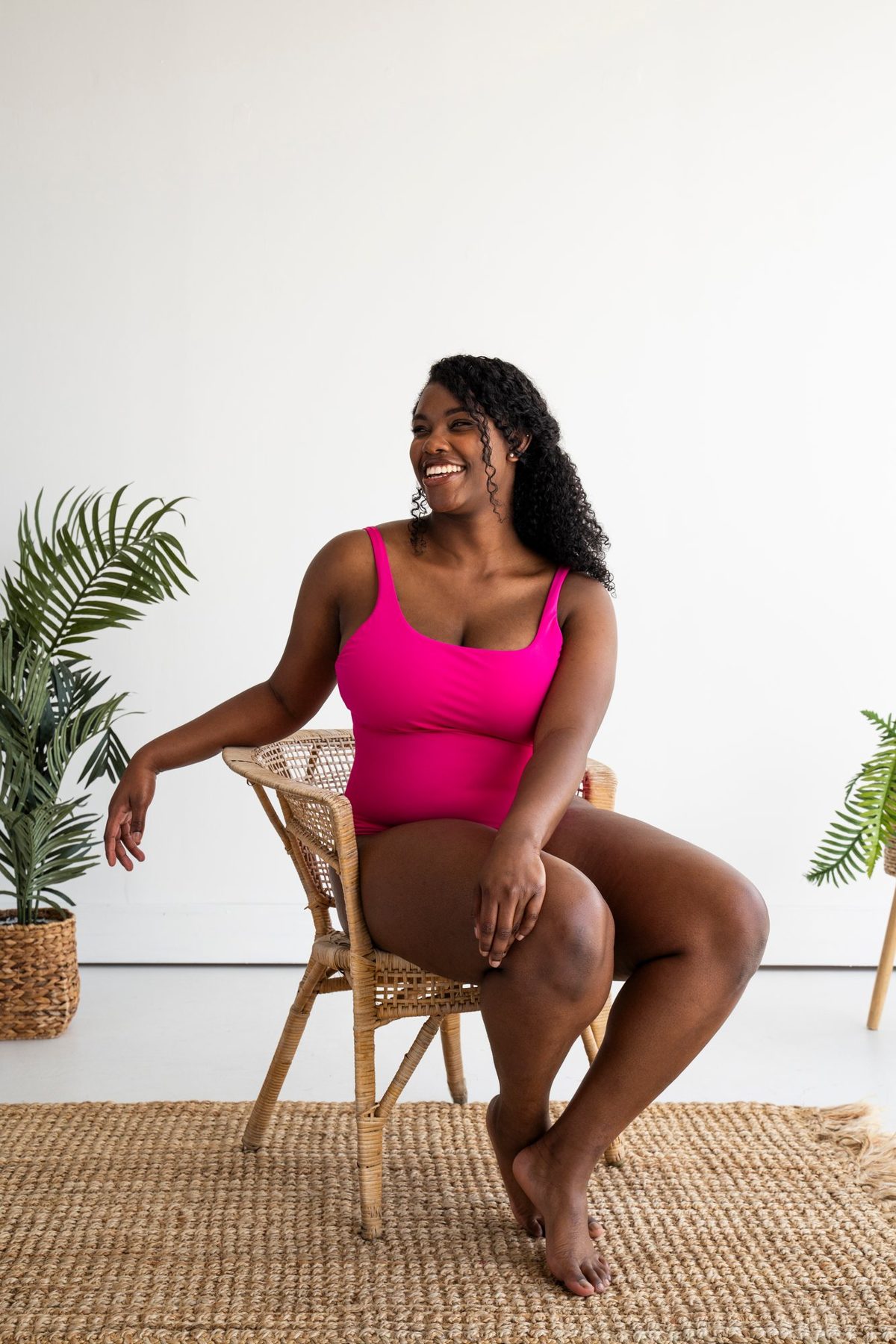 Model in a pink one-piece on a rattan chair with palms