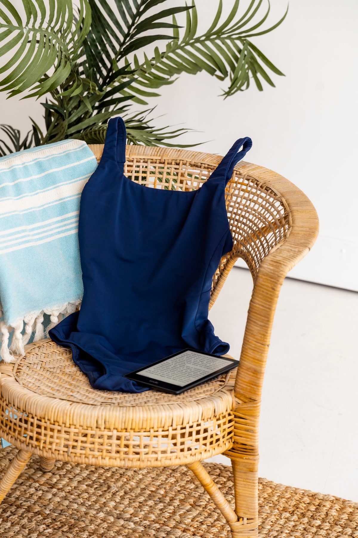 Navy one-piece swimsuit styled on a rattan chair