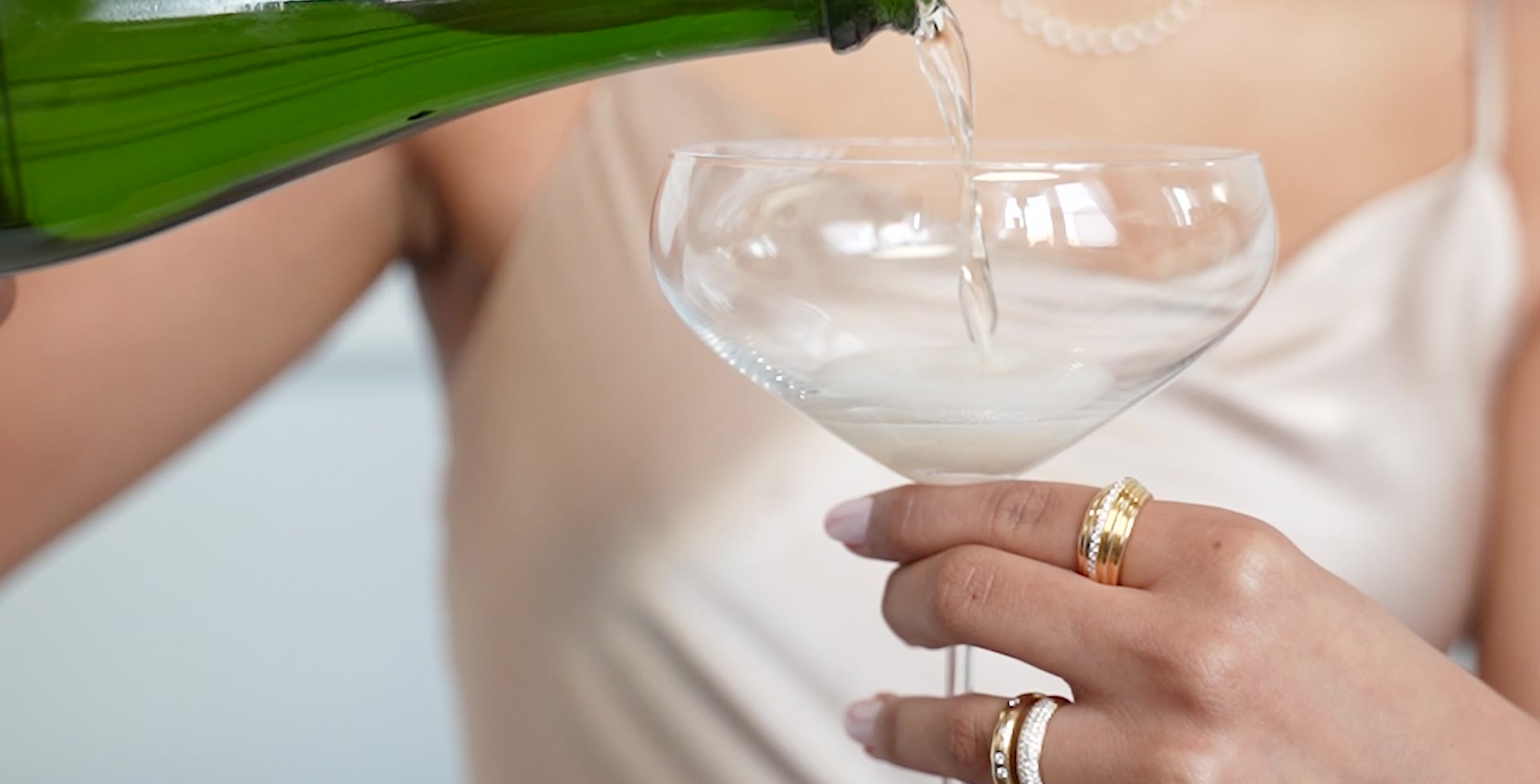 Gold rings on a hand holding a champagne coupe