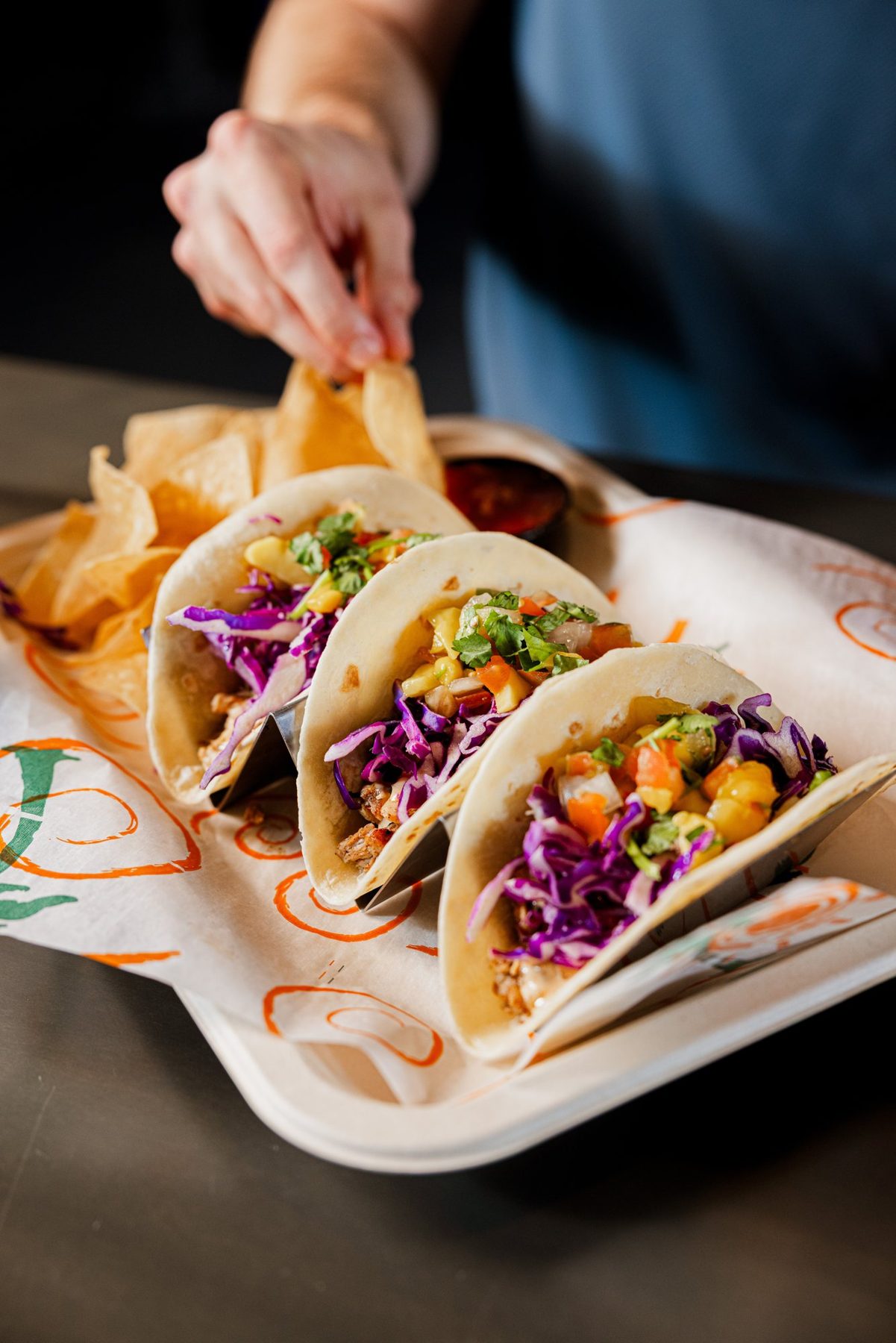 Hand reaching for chips beside a tray of tacos