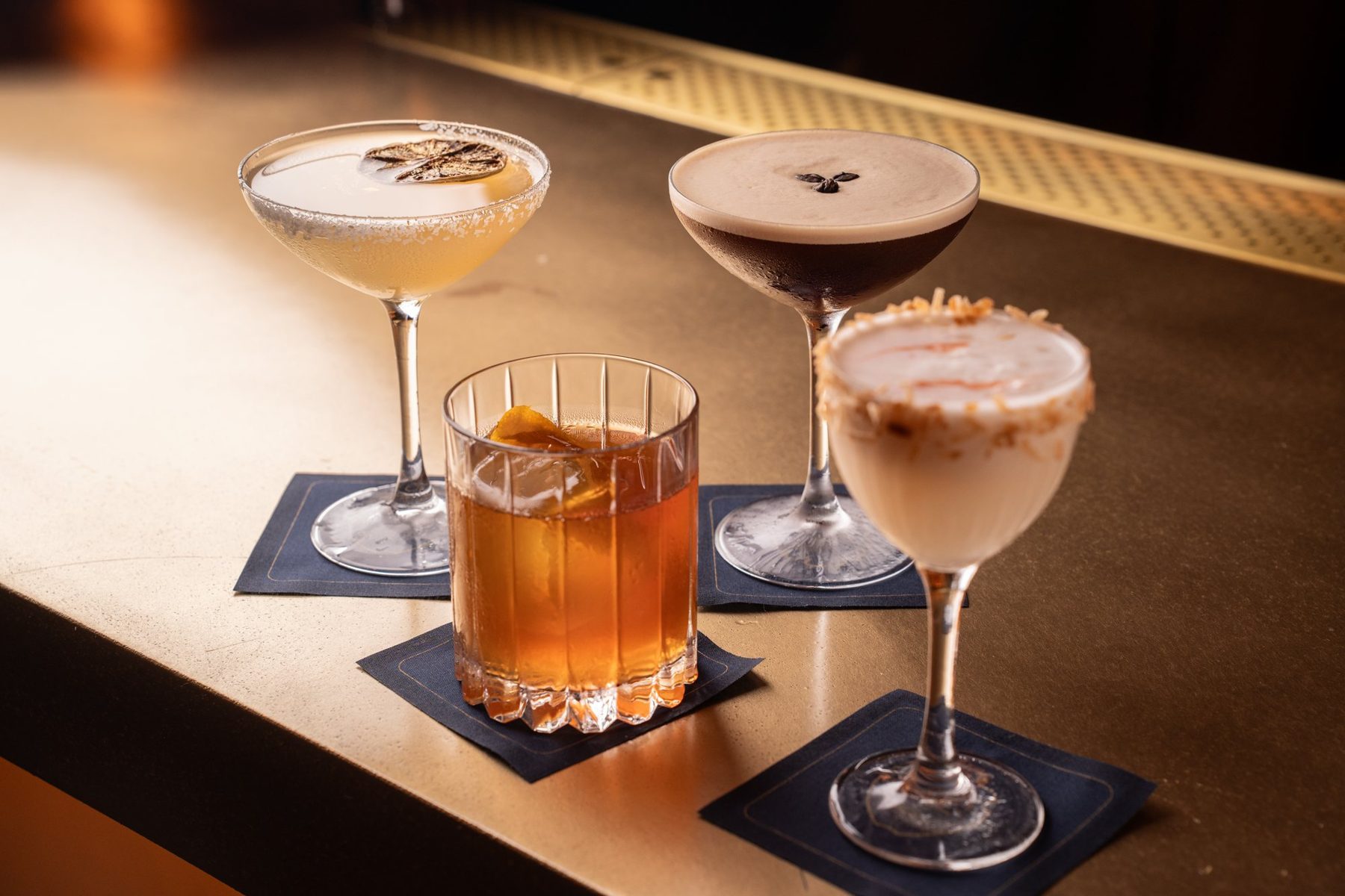 Four cocktails on the bar under warm light