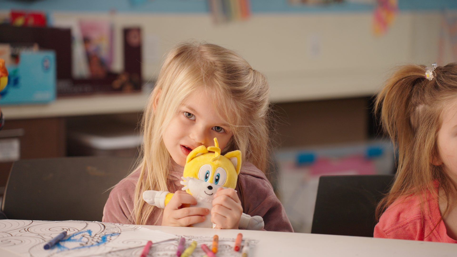 Girl coloring with a plush toy at the activity table