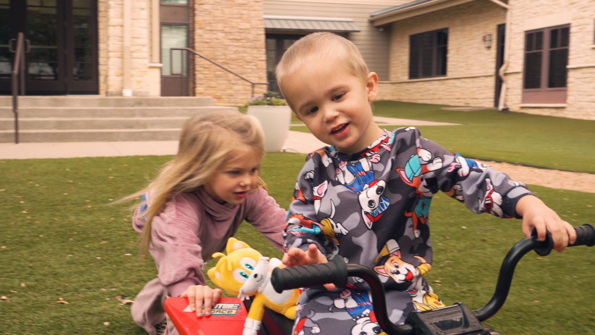 Siblings on a tricycle in the courtyard