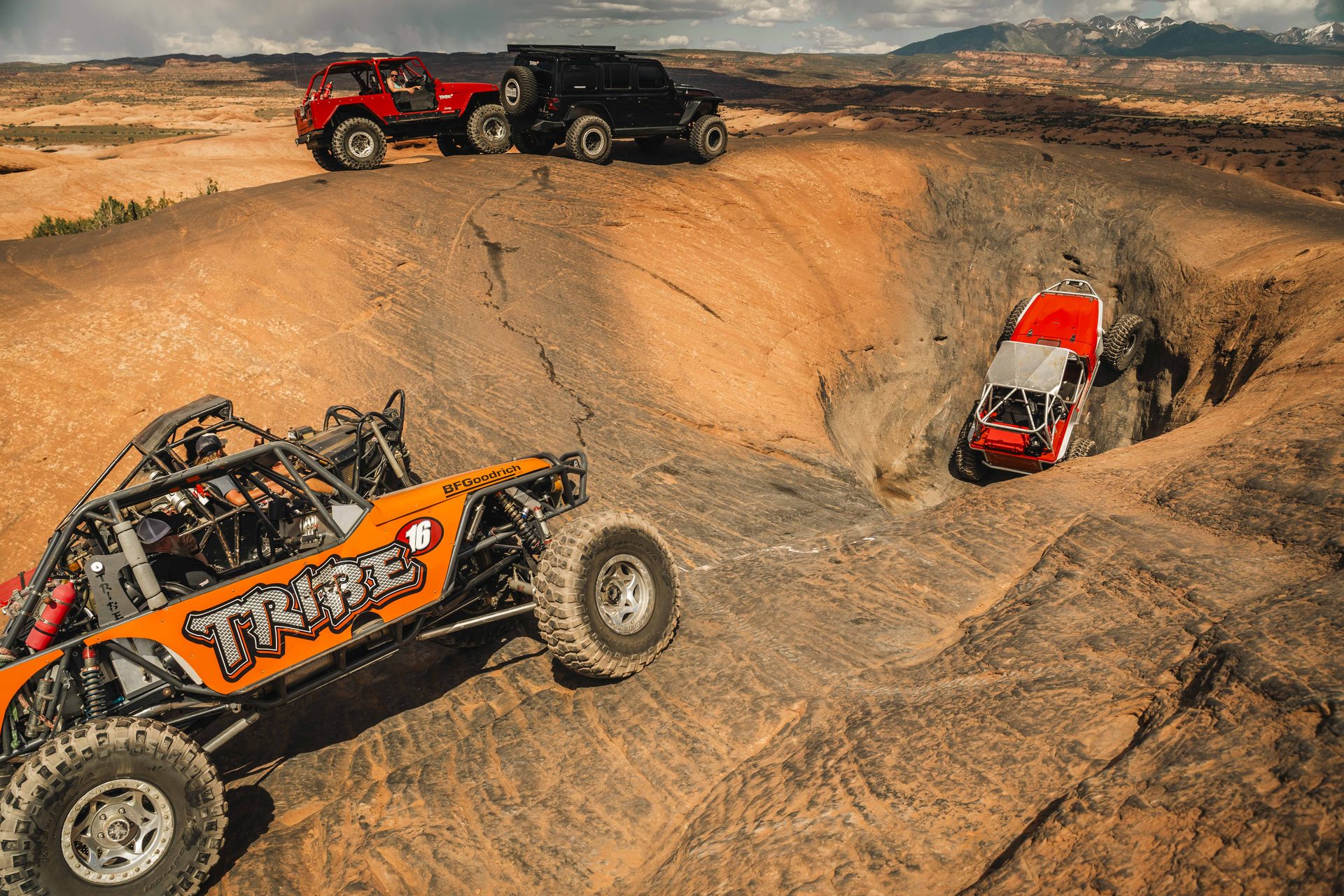 Tribe 16 rock buggy crawling out of a slickrock bowl with Jeeps on the rim