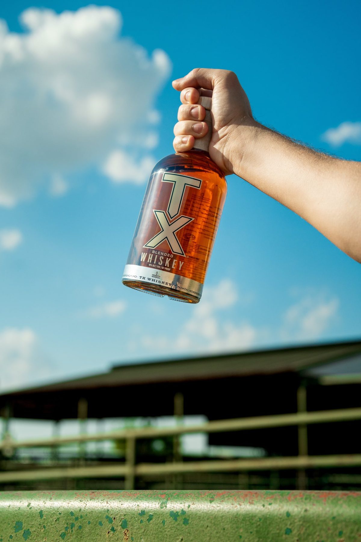 TX Whiskey bottle held up against a blue Texas sky