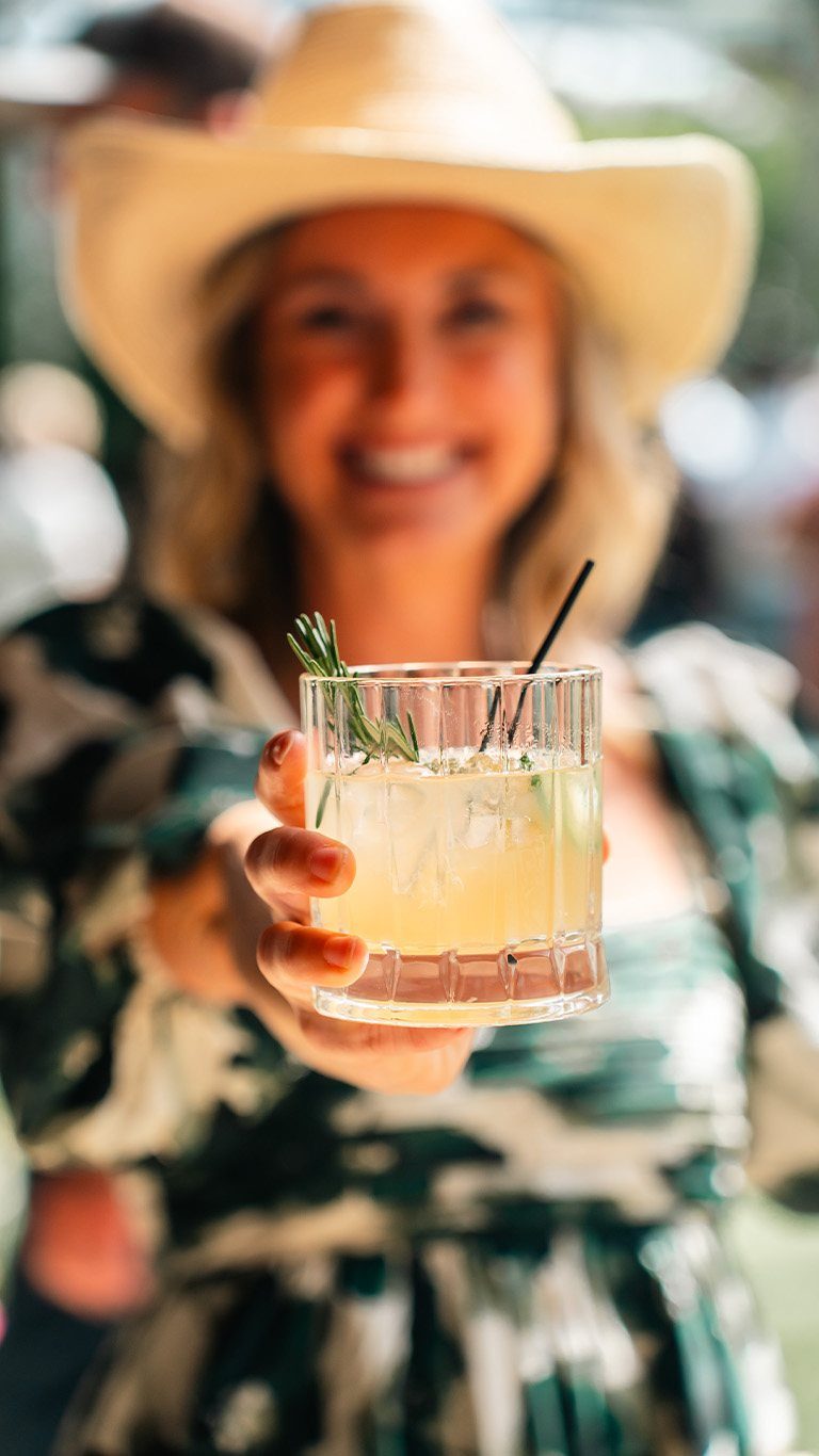 Guest in a cowboy hat holding out a cocktail
