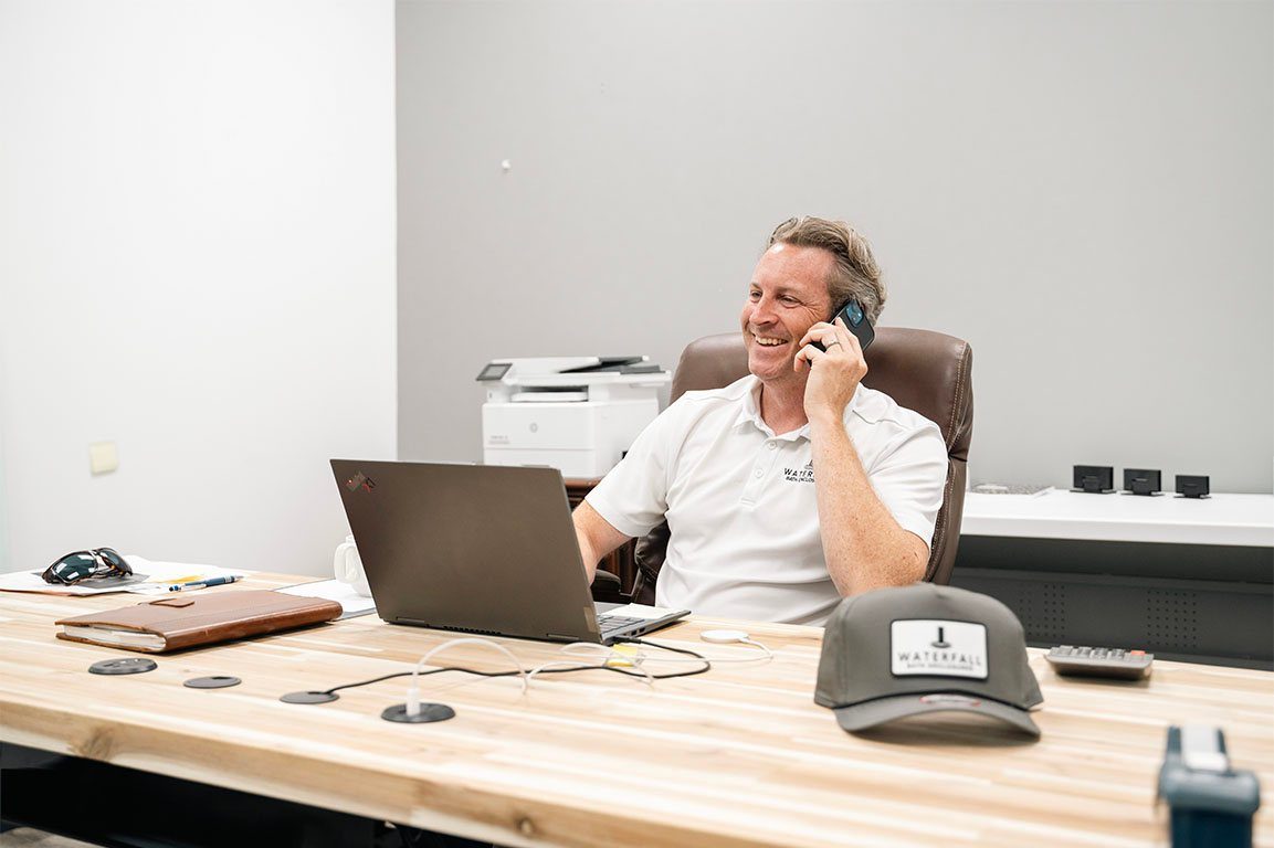 Owner on a phone call at his desk with a Waterfall cap